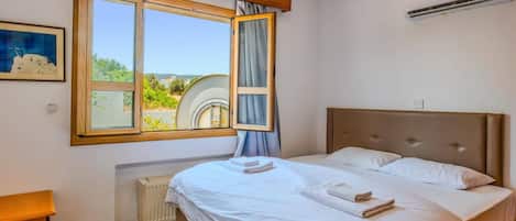 A bedroom with a large bed, a window with curtains, a radiator, and an air conditioning unit.
