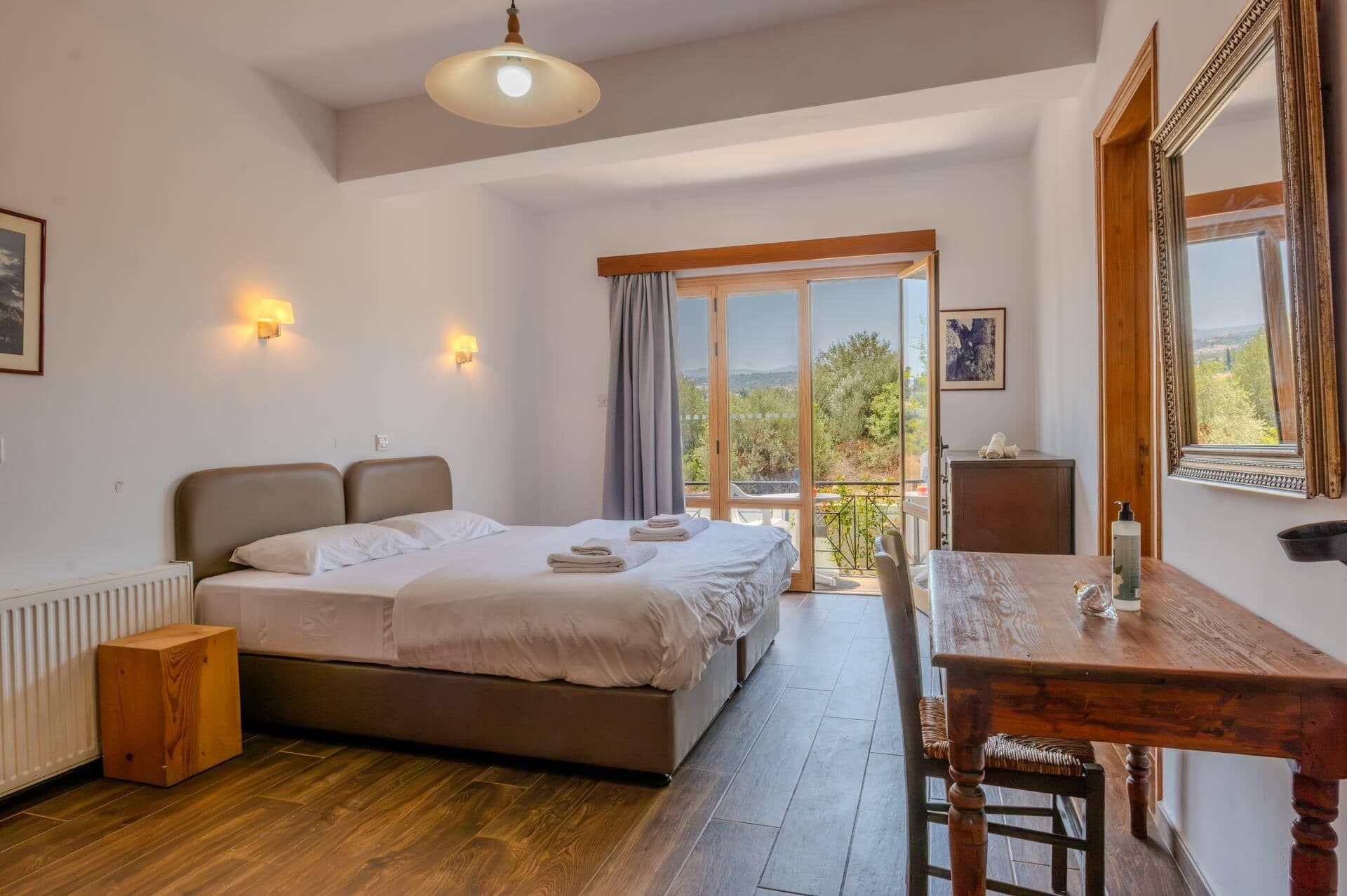 Un dormitorio con cama, una mesa de madera, una silla, un radiador, una ventana con vistas y una lámpara en el techo.