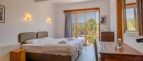 Un dormitorio con cama, una mesa de madera, una silla, un radiador, una ventana con vistas y una lámpara en el techo.