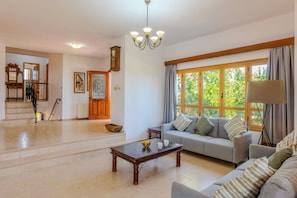 A spacious living room with a sofa, coffee table, and a staircase leading to another level. - Villa Akamas Bayview by Villa Plus (Latchi)
