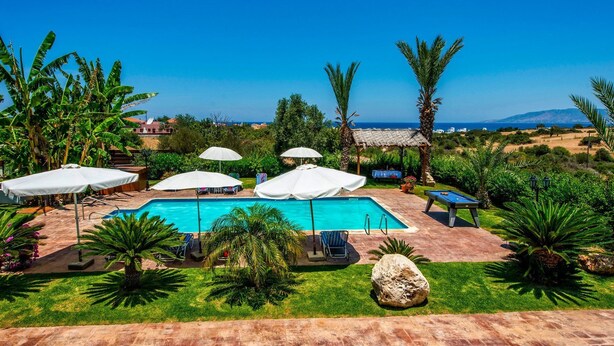 A pool area with umbrellas, lounge chairs, and a view of the sea. - Villa Akamas Bayview by Villa Plus (Latchi)