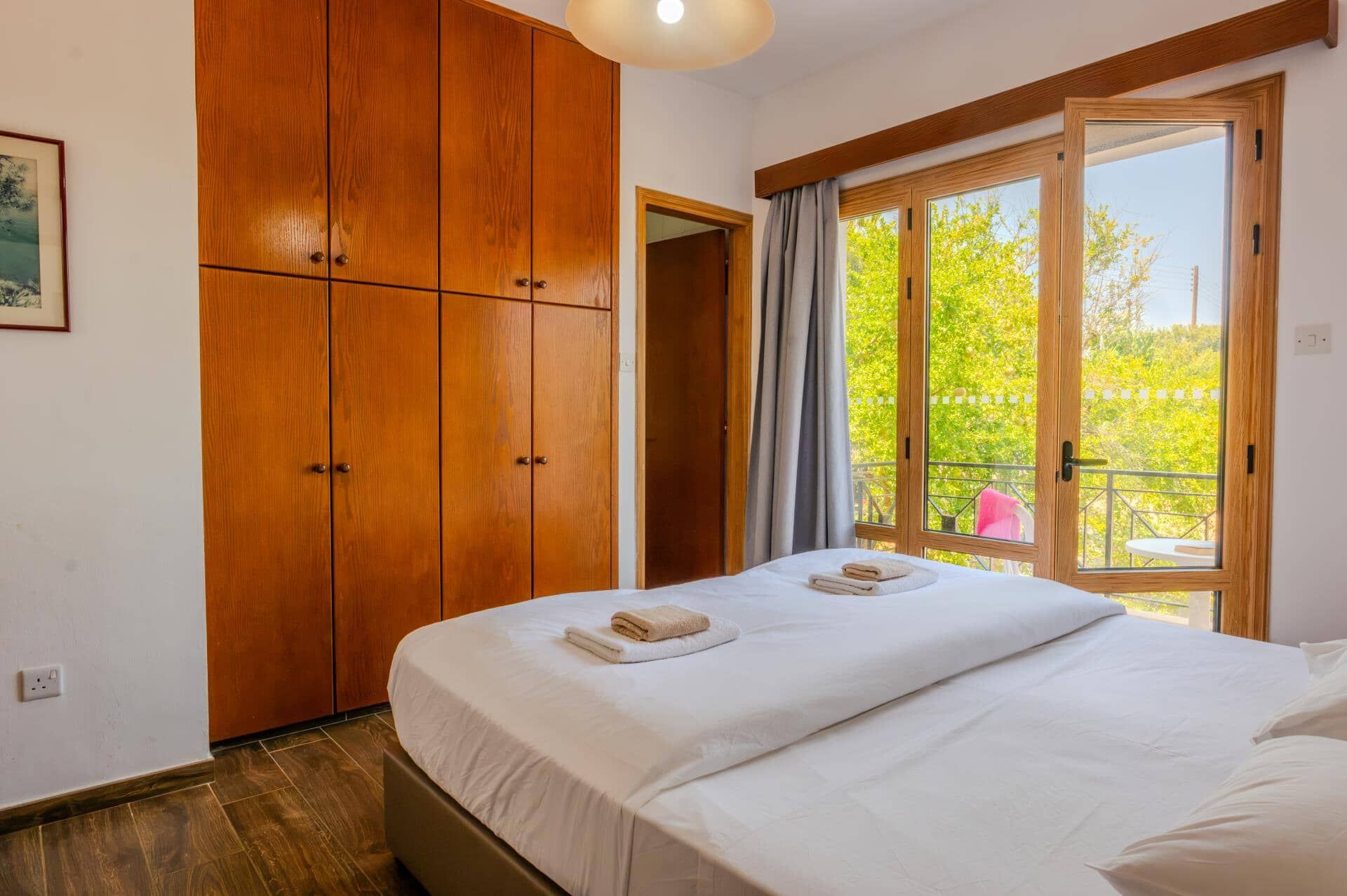 Ein Hotelzimmer mit einem großen Bett, einem Holzschrank und einem Balkon mit Blick auf Grünflächen.