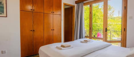 Una habitación de hotel con una cama grande, armario de madera y un balcón con vistas a la vegetación.