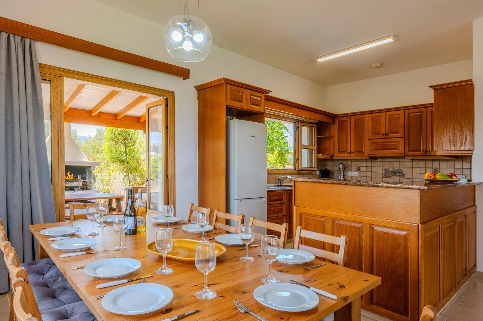 Un comedor con una mesa de madera lista para una comida, una cocina con armarios de madera y vistas al exterior.