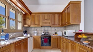 A kitchen with wooden cabinets, a stove, a microwave, and a sink. - Villa Akamas Bayview by Villa Plus (Latchi)