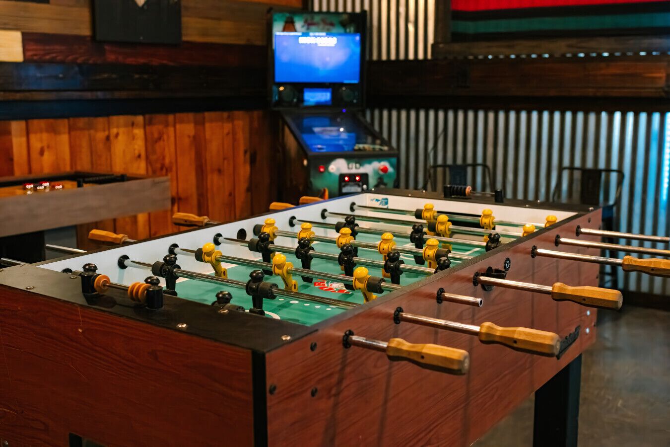 Une table de baby-foot dans une pièce aux murs en bois, avec une télévision en arrière-plan.