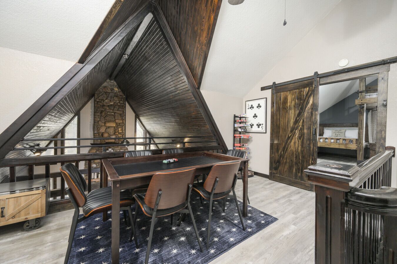 A dining area with a table and chairs, a star-patterned rug, a stone wall, and a wooden ceiling structure.