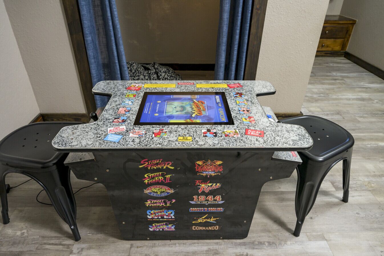 A gaming table with a monitor, two chairs, and various game-related stickers.