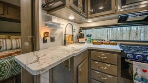 A compact RV kitchen with a stove, sink, and storage cabinets. - Moon Dancer at SOHO Park (Broken Bow)