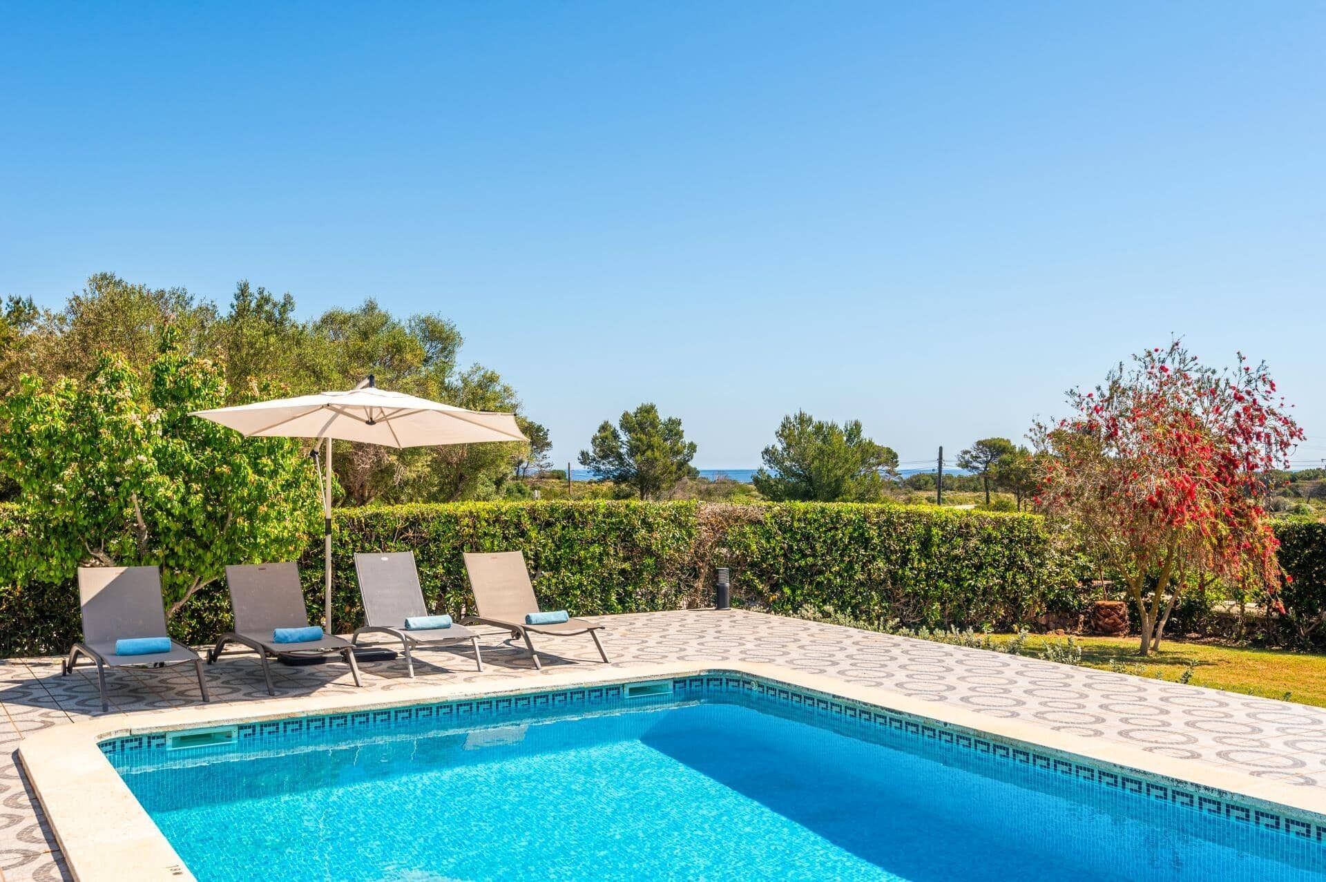 Ein rechteckiger Swimmingpool mit Fliesen umgeben, mit Liegestühlen und einem Sonnenschirm.