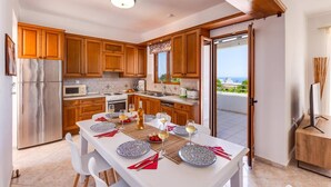 A modern kitchen with wooden cabinets, a stainless steel refrigerator, and a dining area set for a meal. - Villa Kostas Maria by Villa Plus (Episkopi)
