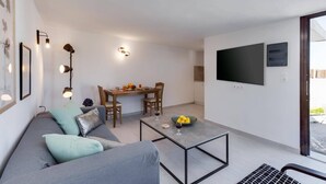 A modern living room with a grey sofa, a coffee table, and a dining area with a table and chairs. - Villa Kostas Maria by Villa Plus (Episkopi)