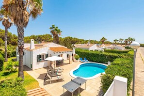 A pool area with lounge chairs and a small table, surrounded by greenery and palm trees. - Villa Jero by Villa Plus (Cap d'Artrutx)