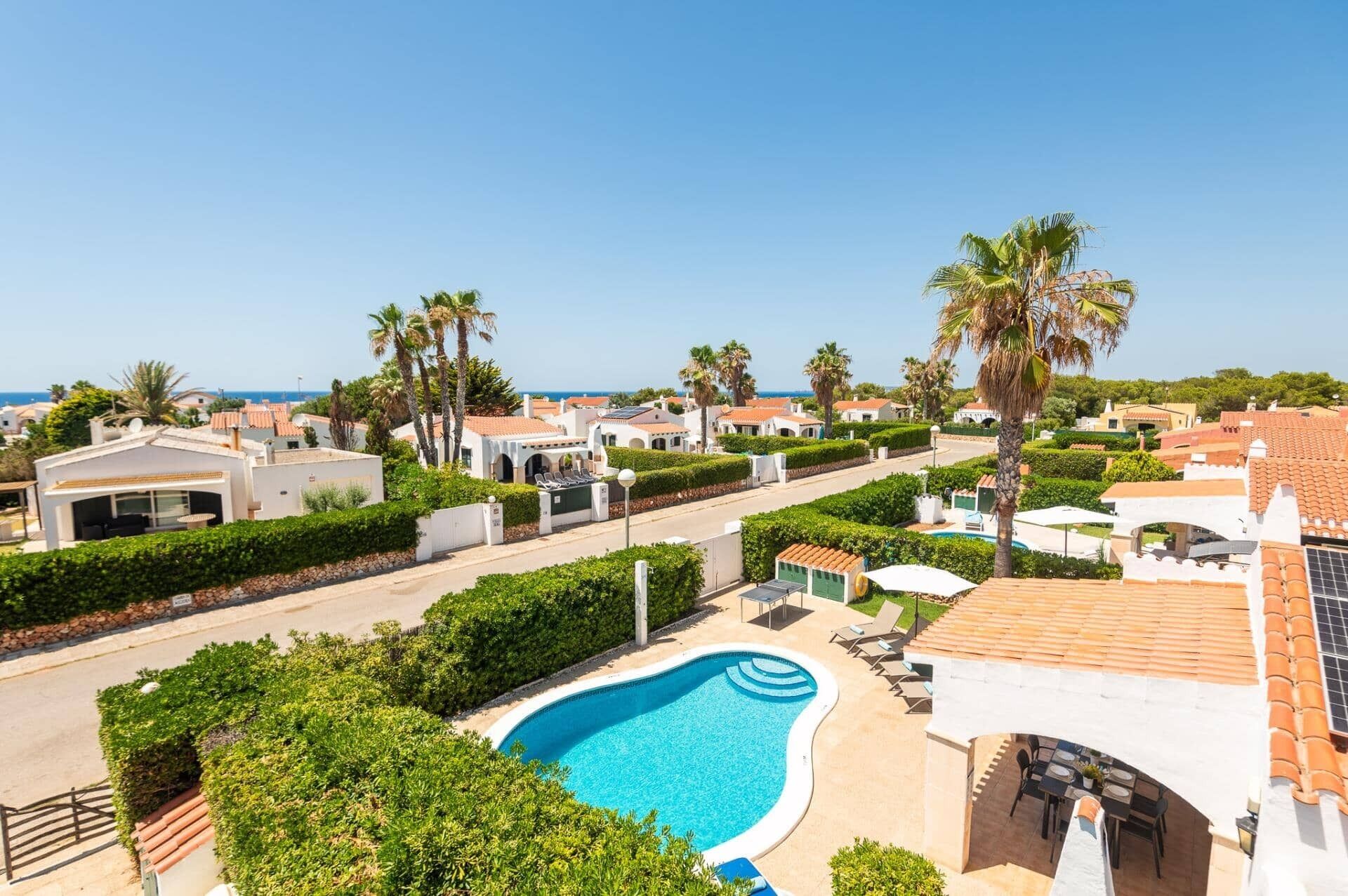 Zona residencial con piscina, palmeras y casas con techos de tejas rojas.