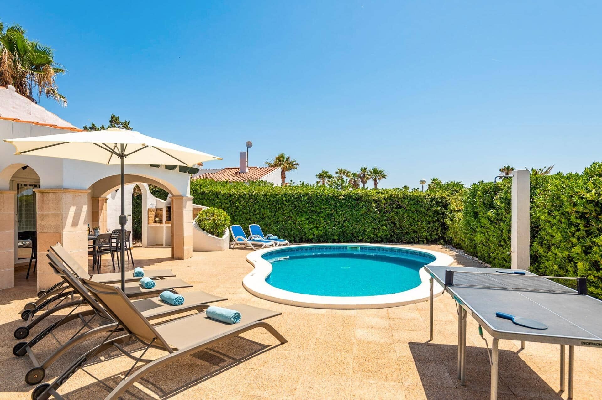 A pool area with lounge chairs, a table tennis table, and a covered seating area.