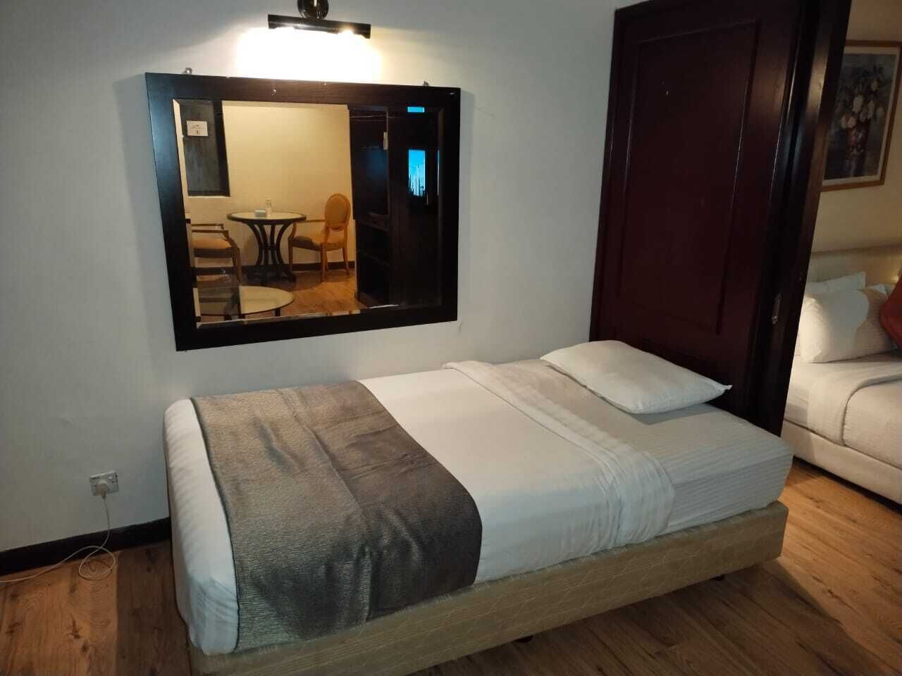 Una cama individual con cabecera, una mesita de noche, un espejo y suelo de madera.