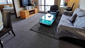 A modern hotel room with a sofa, a glass coffee table, a TV, and a large window with curtains. - The Hotel Apartment At Times Square (Kuala Lumpur)