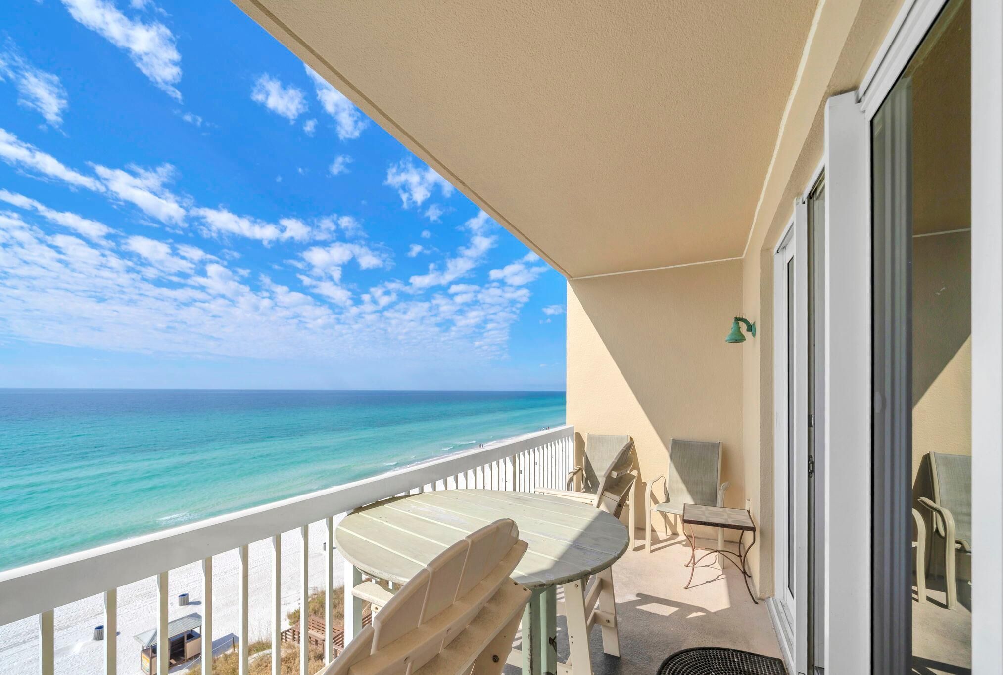 A balcony with a table and chairs, overlooking a beach and ocean.
