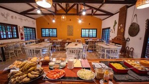 A dining area with multiple tables and chairs, a buffet with various food items, and a brick oven. - Pousada das Cavernas (Iporanga)