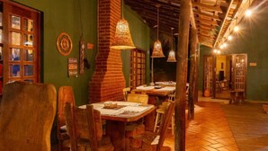 A restaurant with wooden tables and chairs, hanging wicker lamps, and a brick wall. - Pousada das Cavernas (Iporanga)