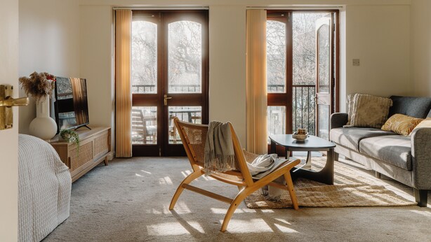 Ein gemütliches Wohnzimmer mit einer Couch, einem Sessel, einem kleinen Tisch und einem Fernseher auf einer Holzkommode.
