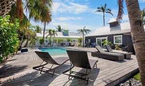 Una terraza de madera con sillones de descanso y una piscina.