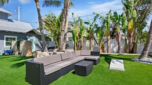 Un espacio exterior moderno con un sofá modular, una mesita y una jardinera de piedra.