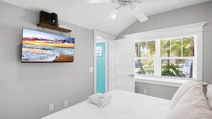 Une chambre à coucher avec un lit, un téléviseur fixé au mur, un ventilateur de plafond et une fenêtre donnant sur un paysage verdoyant.