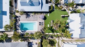 Vue aérienne d’un complexe hôtelier doté d’une piscine, de palmiers et d’une zone aménagée avec des chaises longues.