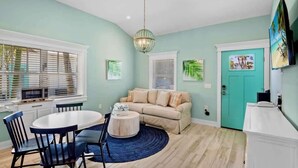 Un salon avec une table ronde, un canapé beige et une porte de couleur turquoise.