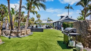 Un jardin avec une piscine, un barbecue et des palmiers.