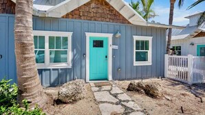 Une maison de plain-pied avec une porte d’entrée turquoise, des volets blancs et un petit porche.