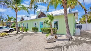 A light green building with a metal roof, surrounded by palm trees and a gravel driveway. - New! Perfect Location! Heated Pool~Steps to Beach! (Holmes Beach)