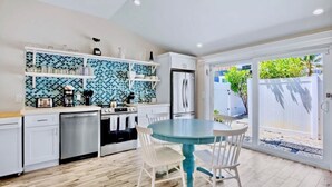 A modern kitchen with white cabinets, a blue tiled backsplash, and a round table with chairs. - New! Perfect Location! Heated Pool~Steps to Beach! (Holmes Beach)