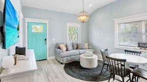 A modern living room with a teal door, grey sofa, round coffee table, and a dining area with a white table and dark chairs. - New! Heated Pool~Steps to the Beach/Shops~Starfish (Holmes Beach)