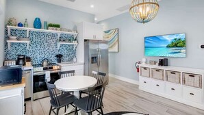 A modern kitchen with a dining area, featuring a white refrigerator, stove, and microwave. There is a TV mounted on the wall, and a chandelier hangs from the ceiling. - New! Heated Pool~Steps to the Beach/Shops~Starfish (Holmes Beach)