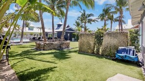 A well-maintained outdoor area with a pool, palm trees, and a stone wall. - New! Heated Pool~Steps to the Beach/Shops~Starfish (Holmes Beach)