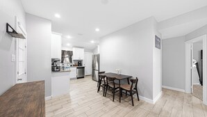 A modern kitchen with white cabinets, a stainless steel refrigerator, and a dining area with a wooden table and chairs. - Luxury Remodeled 3 Bed/2 Bath Home with Patio Deck (Mansfield)
