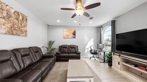 A modern living room with a leather sofa, a recliner, a coffee table, a flat-screen TV, and a ceiling fan. - Luxury Remodeled 3 Bed/2 Bath Home with Patio Deck (Mansfield)