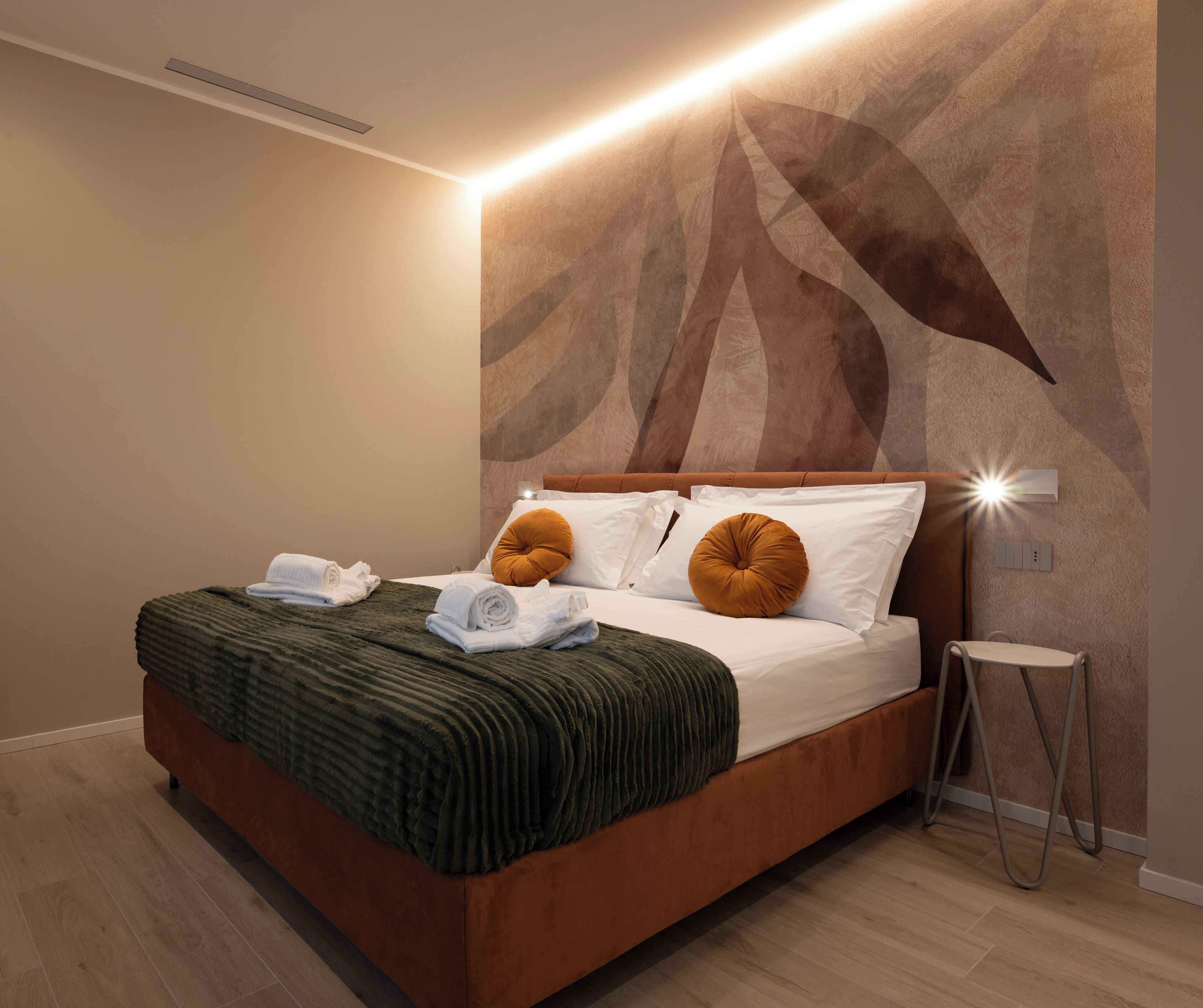 A modern hotel room with a large bed, a headboard with integrated lighting, a small bedside table, and a wall-mounted light fixture.