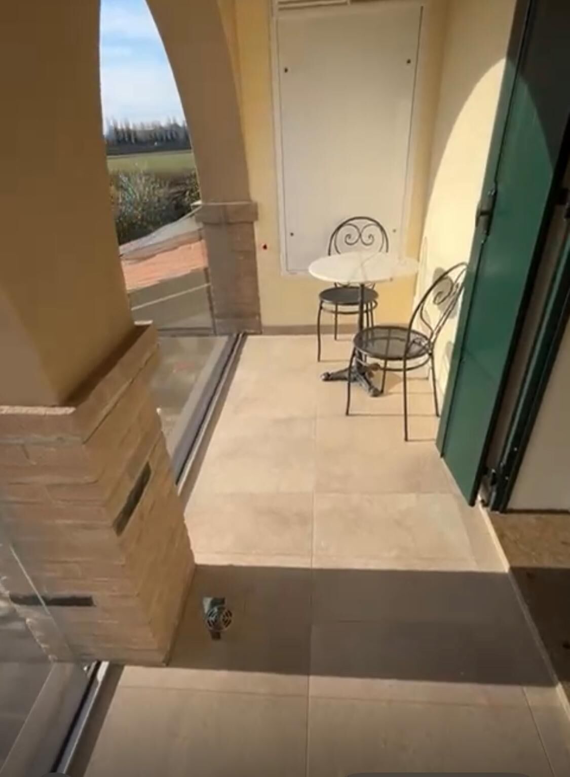 A balcony with a view of the outdoors, a small table with chairs, and a door with a window.