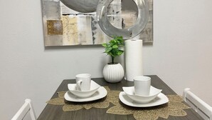 Een eethoek met een tafel gedekt voor twee personen, een decoratieve spiegel en een potplant.