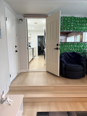 An open door leading to a kitchen with a wooden floor, a dining area with a table and chairs, and a dark blue chair in the foreground. - Relaxing Cozy Back House with Backyard (Upland)