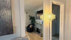 Een kamer met een grote spiegel, een gestoffeerde fauteuil, een vloerlamp en een dressoir met lades.