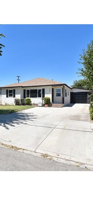 A single-story house with a front driveway, a garage, and a small front yard with a lawn and a few shrubs. -  Relaxing Cozy Back House with Backyard (Upland)