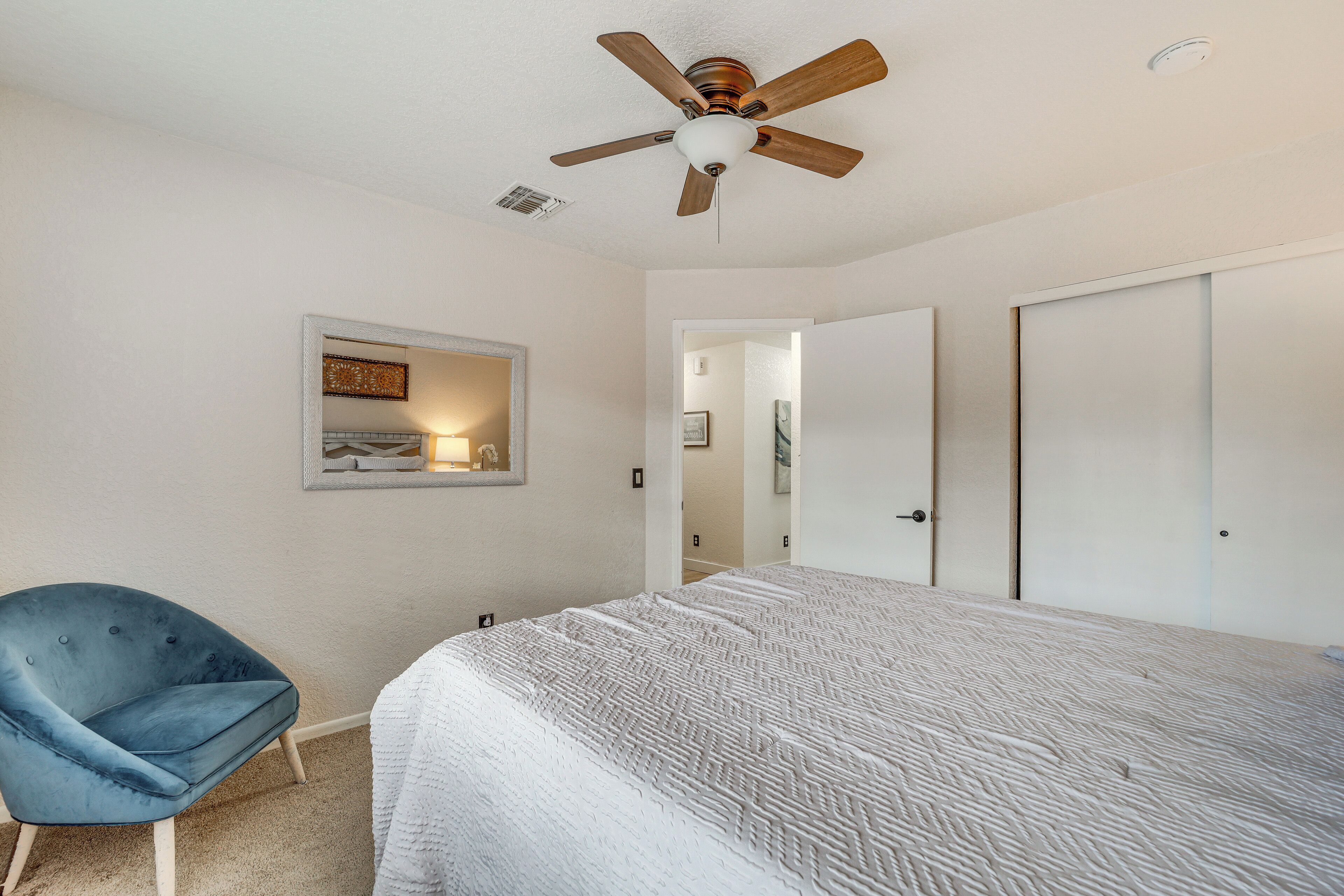 A bedroom with a bed, a ceiling fan, a chair, and a door leading to another room.