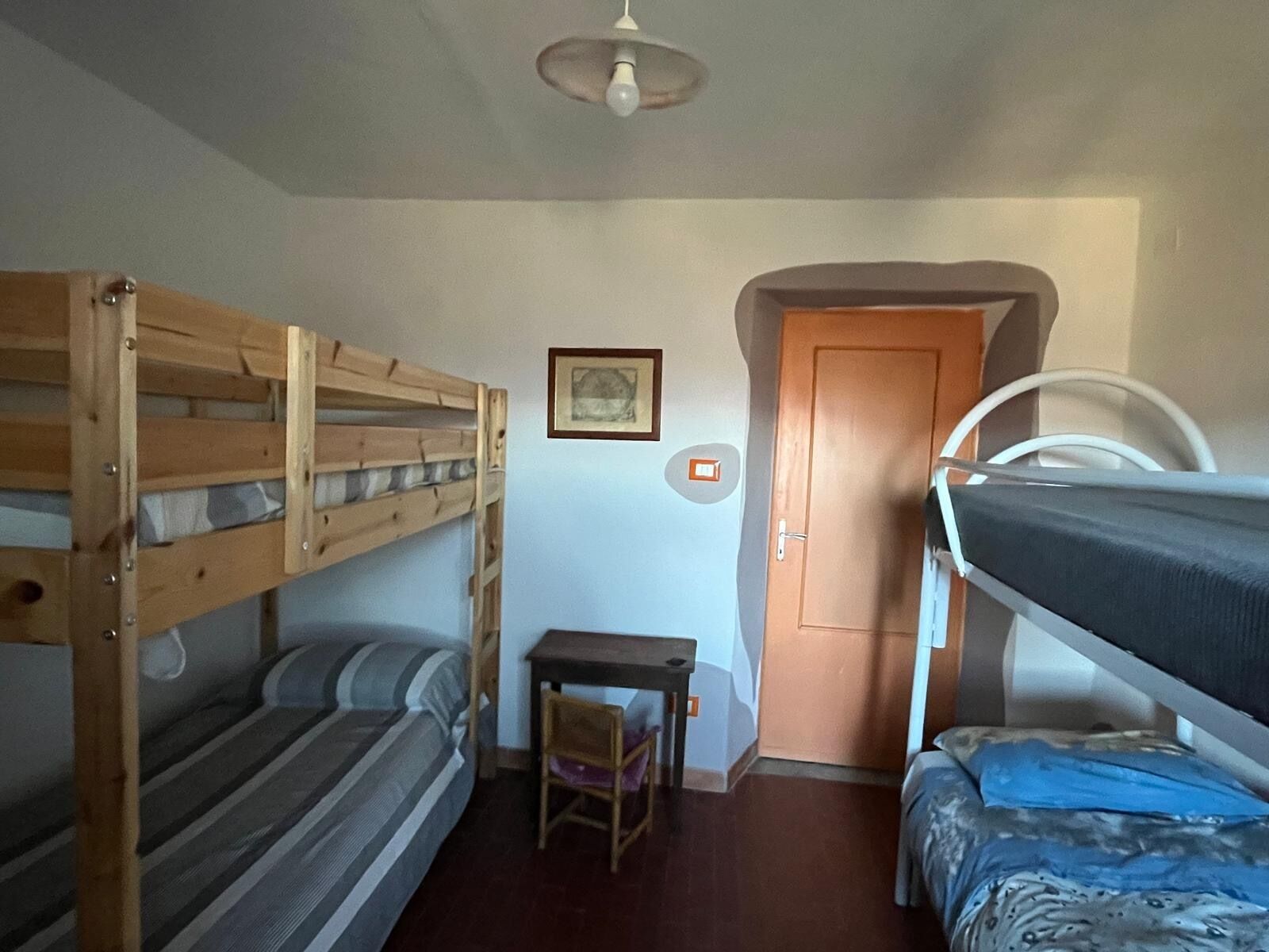 Une chambre de dortoir avec des lits superposés, une petite table, une chaise, une porte et un ventilateur de plafond.