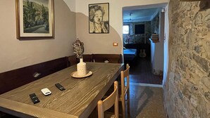 Ein Essbereich mit einem Holztisch, Stühlen und einer Blumenvase als Mittelstück. An den Wänden befinden sich gerahmte Bilder und rechts eine Steinwand.