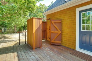 A wooden deck with a covered outdoor shower and a door to a building. - Summer Beach Pass: Wooded Martha's Vineyard Escape (Vineyard Haven)
