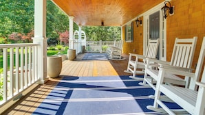 A covered porch with white rocking chairs, a wooden ceiling, and a view of a garden. - Summer Beach Pass: Wooded Martha's Vineyard Escape (Vineyard Haven)